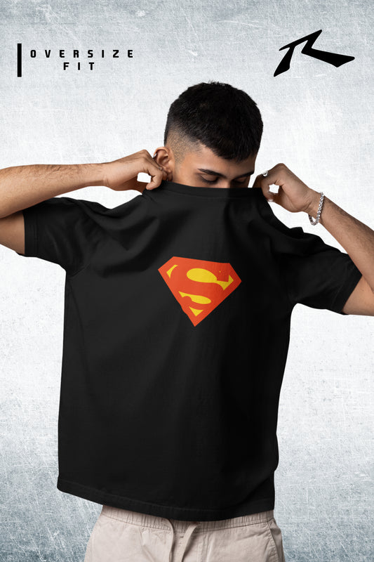 Person wearing a black t-shirt with a Superman logo, posing against a gray background.